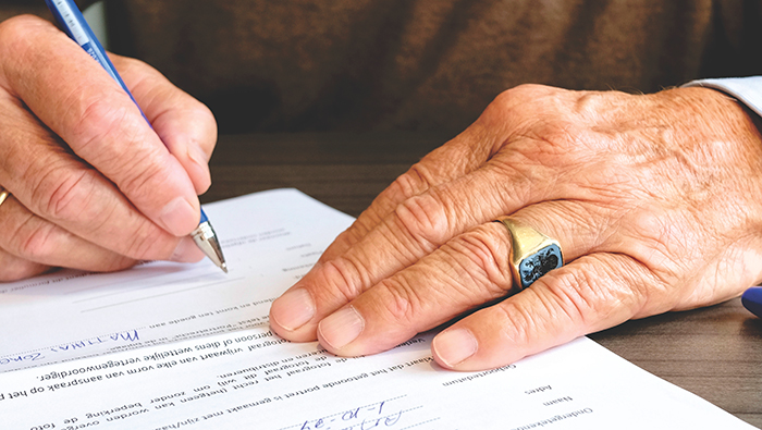 The hands of an old person signing a legal document