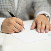 An image of hands holding a pen and writing on a blank sheet of paper.