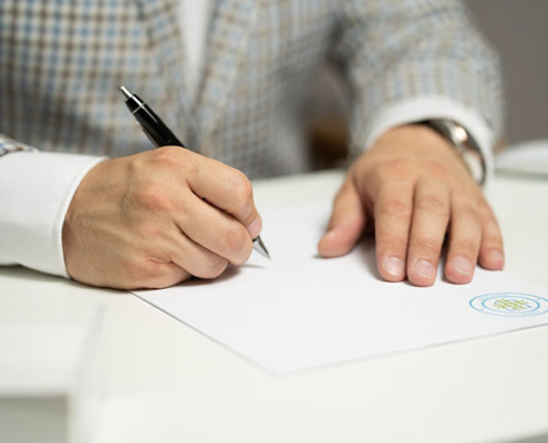 An image of hands holding a pen and writing on a blank sheet of paper.